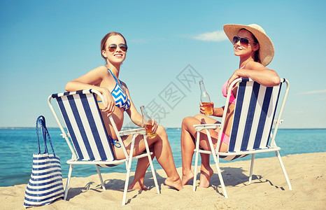 闲暇坐暑假,旅行人们的快乐的女人海滩的休息室里喝啤酒日光浴背景