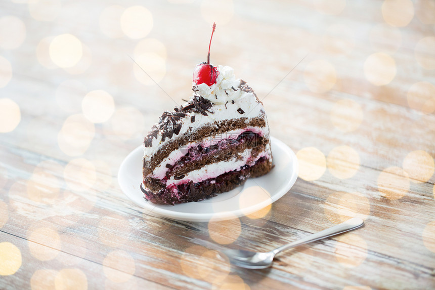 食物,垃圾食品,烹饪,烘焙假日块美味的樱桃巧克力层蛋糕茶托与勺子木桌上的假日灯光背景图片