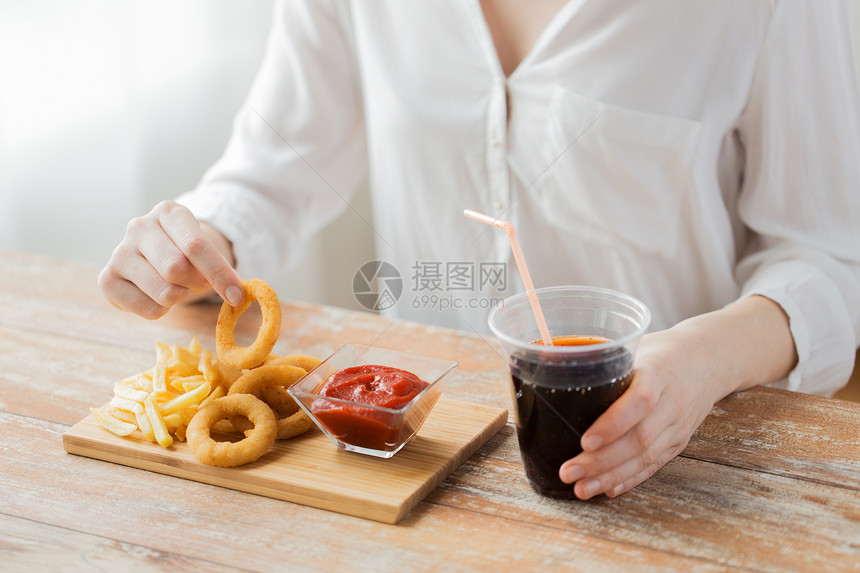 快餐,人健康的饮食观念密切妇女吃油炸鱿鱼戒指,炸薯条与番茄酱饮用可口可乐木桌上图片