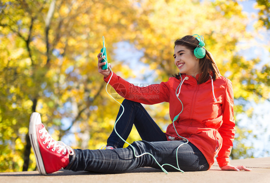 技术,生活方式人们的微笑的轻妇女十几岁的女孩,带着智能手机耳机,秋天的公园背景下户外听音乐图片