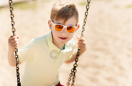 快乐的小男孩戴着太阳镜儿童游乐场荡秋千图片