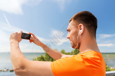音乐与海微笑的年轻人与智能手机耳机听音乐夏季海边背景