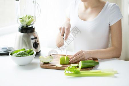 黄瓜切条器饮食人的轻妇女与搅拌机切绿色蔬菜排奶昔冰沙家背景