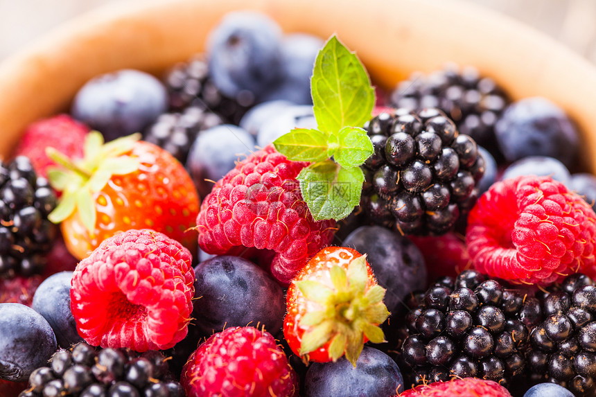 夏天的野生浆果破旧的木制背景上把覆盆子,草莓,黑莓蓝莓放碗里图片