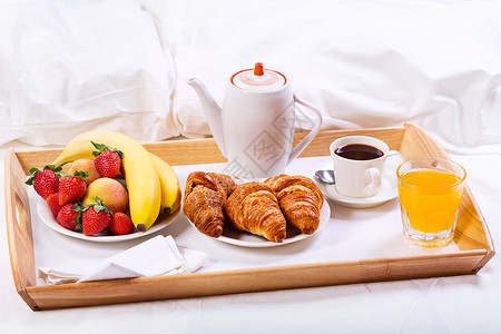 床上吃早餐托盘上咖啡牛角包水果背景图片