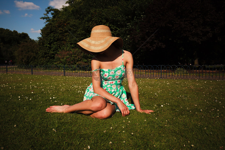 个穿着连衣裙帽子的轻女人坐公园的草地上图片