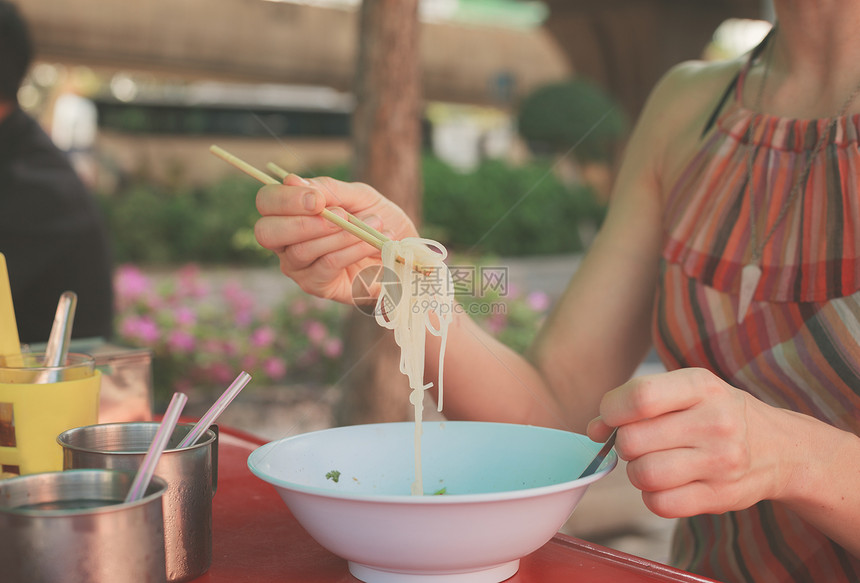 一个年轻女人坐街上的张桌子上吃条图片