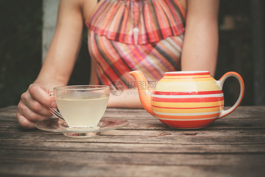 一个年轻穿着夏装的轻女人正木桌上喝茶图片