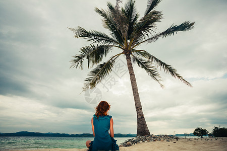 个轻的女人坐热带海滩上的棕榈树下背景图片