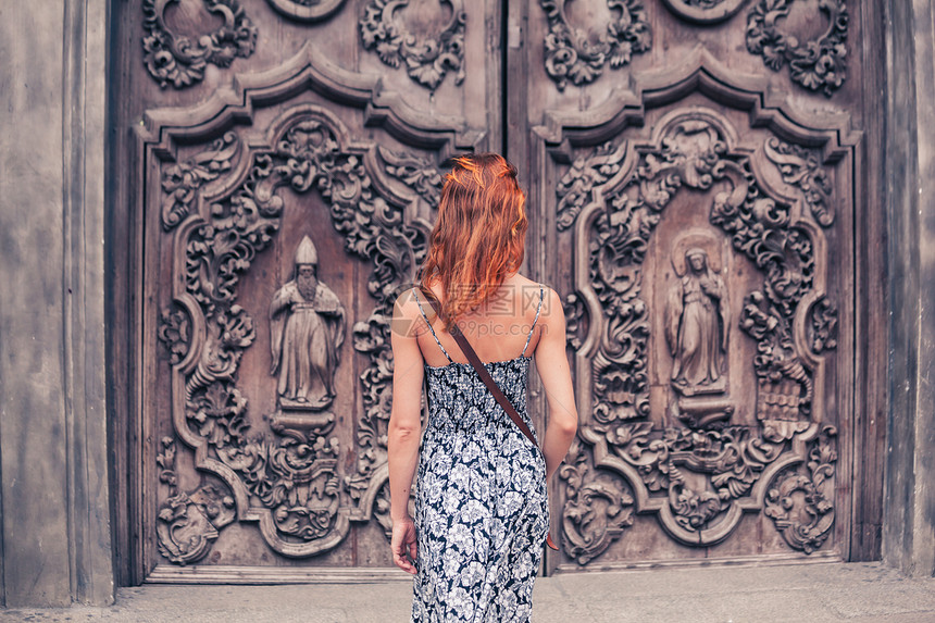 一个年轻的女人站教堂外,扇装饰精美的门图片