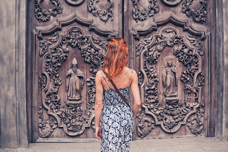 一个年轻的女人站教堂外,扇装饰精美的门高清图片