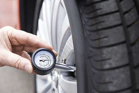 用量规检查汽车轮胎压力的人员特写图片