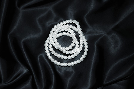 白色珍珠项链上的黑色丝绸特写背景图片