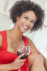 个美丽的快乐混合种族非裔美国女孩轻女子穿着红色的衣服,家里喝红酒图片