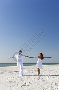 中快乐的男女浪漫的夫妇穿着白色的衣服个荒凉的热带海滩上跳舞,明亮的蓝天图片