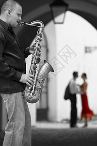 小夜曲黑白照片街头音乐家演奏他的萨克斯管,而浪漫的夫妇可以看背景中的焦点,女人穿着红色的衣服背景