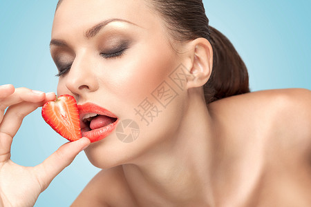 个漂亮的女孩用诱人的舌头舔着颗红色多汁的草莓图片