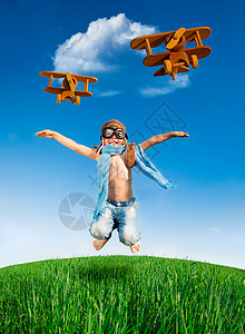 快乐的孩子穿着件飞行员的衣服,绿色的田野上着蓝天跳跃暑假图片