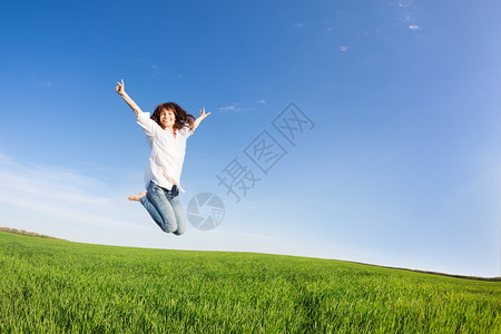快乐的女人绿色的田野上跳跃着蓝天暑假图片