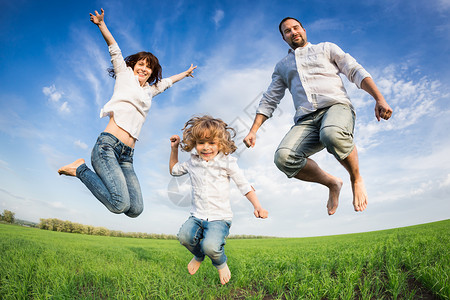 快乐活跃的家庭跳跃绿色的田野抗蓝天暑假图片