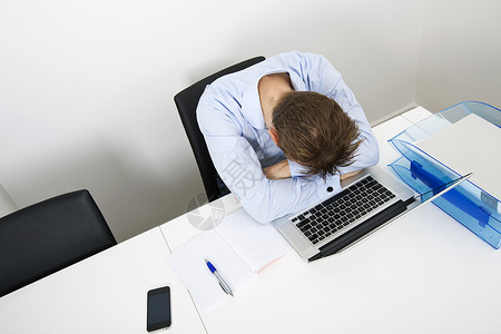 势可挡的疲惫的商人睡办公室桌子上的笔记本电脑上背景