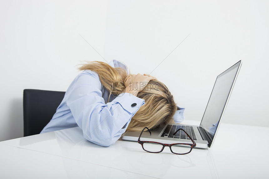 疲惫的女商人把头靠办公室的笔记本电脑上图片