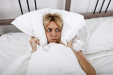 轻的女人床上用枕头盖住耳朵图片