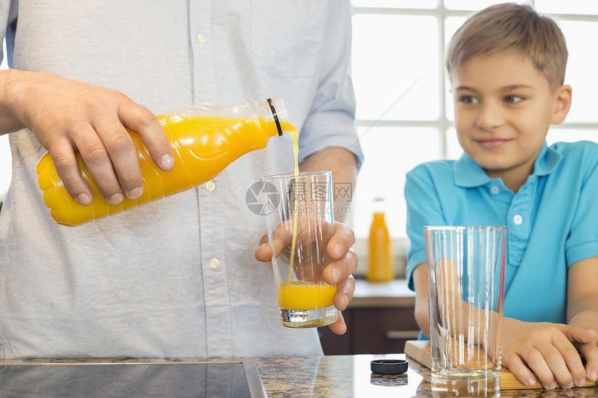 父亲的中段厨房为儿子供应橙汁图片