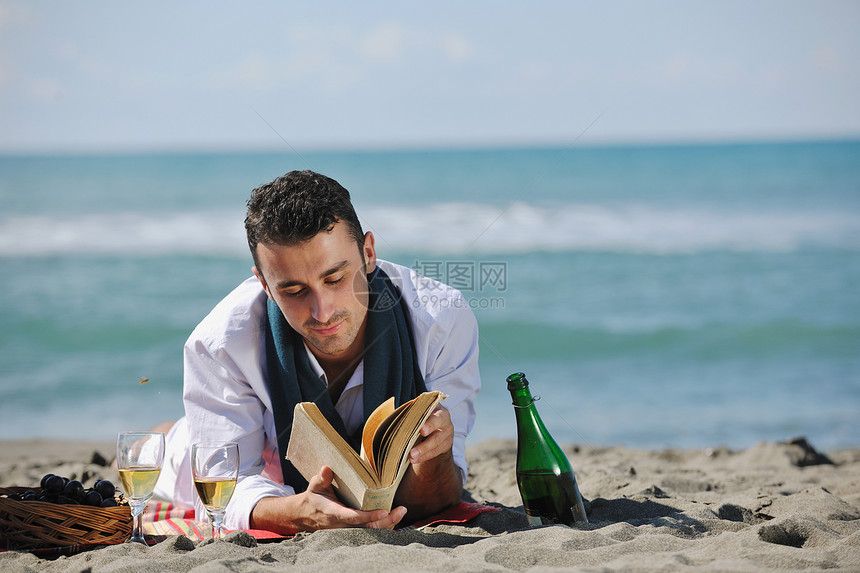 轻人美丽的晴天海滩上放松,同时阅读代表暑期学校教育理念的书籍图片