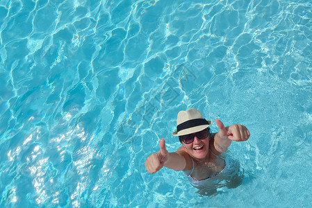 带着帽子太阳镜的快乐微笑的女人热带度假村的游泳池里图片
