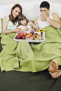 快乐的轻家庭早上床上吃早餐图片