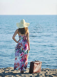 海滩上着手提箱旅行袋的女人代表着异国情调奢华的逃避自由图片