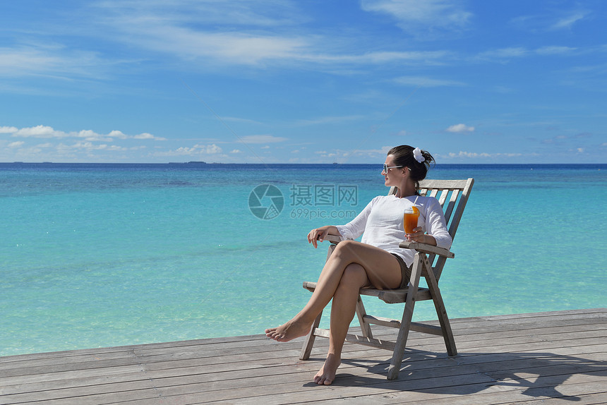 穿着比基尼的漂亮轻女人躺躺椅上,海边喝杯图片