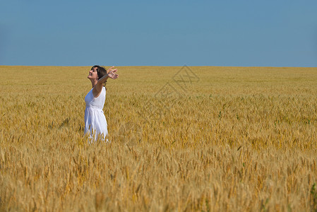 轻的女人站麦田里跳跃奔跑,夏天的背景蓝天,代表着健康的生活农业理念图片