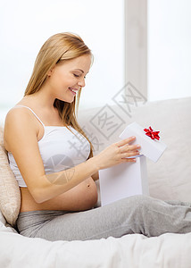 怀孕,母亲庆祝微笑的孕妇坐沙发上,打开礼品盒图片