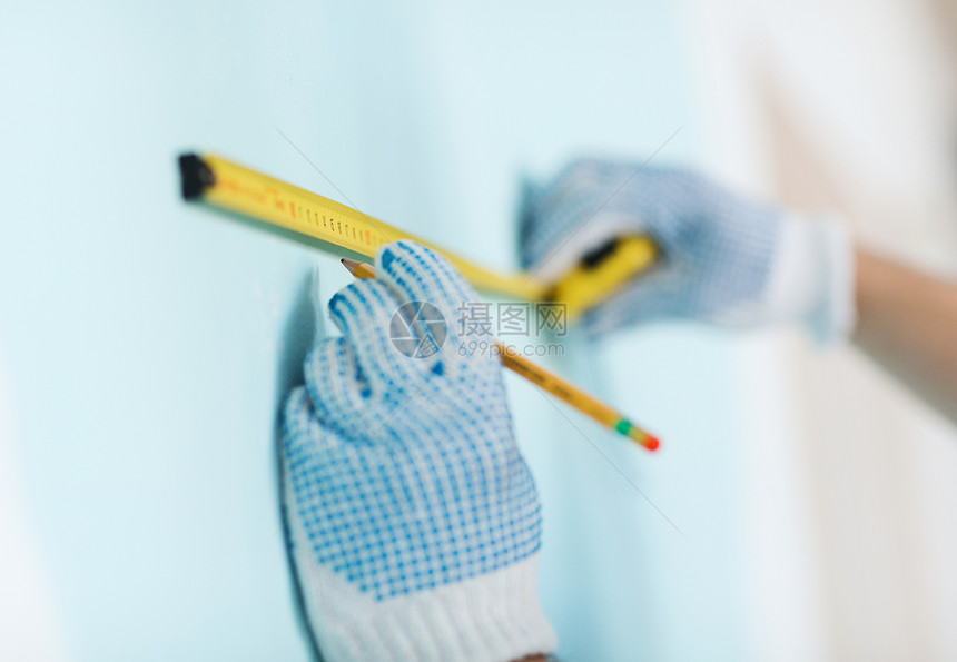 修理建筑家庭用胶带测量墙壁的手套中男的特写图片