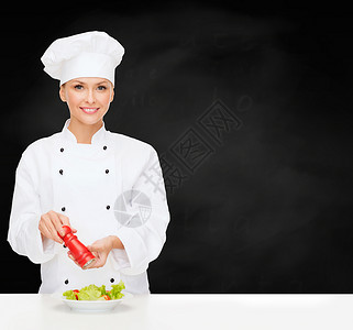 烹饪食物微笑的女厨师,厨师包师准备沙拉与盐胡椒粉磨坊图片