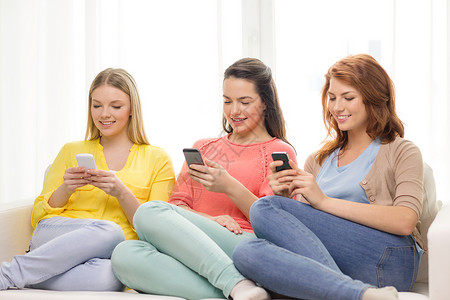 三个微笑的女孩在家里用智能手机图片