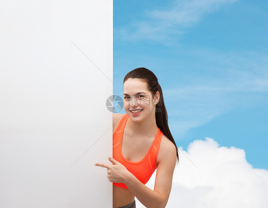 微笑的十几岁女孩穿着运动服,手指指向白色空白板图片