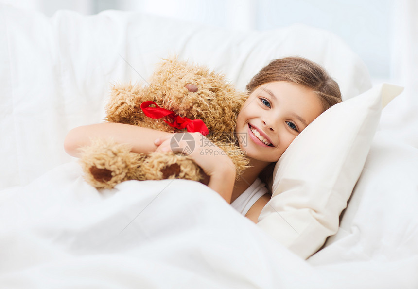 健康美丽的小女孩带着泰迪熊睡家里图片