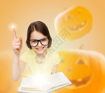 教育,假期,童,视觉人的微笑的小女孩戴着眼镜,带着万节南瓜背景的魔法书图片