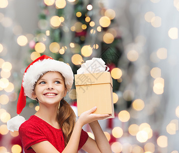 诞节,假日,童人的微笑的女孩诞老人帮助帽子与礼品盒诞树灯光背景图片