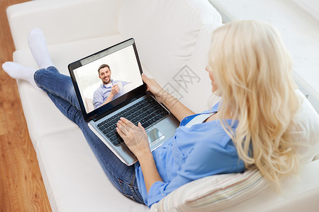 家庭,技术,沟通人的微笑的女人坐沙发上,家里用笔记本电脑聊天图片