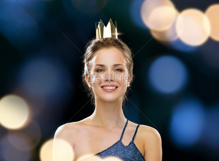 人,假日,皇室,庆祝魅力微笑的女人穿着晚礼服,戴着金色的皇冠黑色背景上的夜灯背景图片