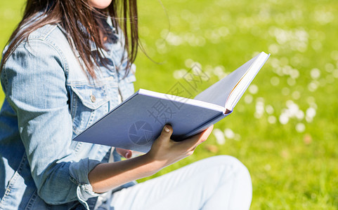 生活方式,暑假,教育,文学人的近距离微笑的轻女孩阅读书籍坐公园的草地上图片