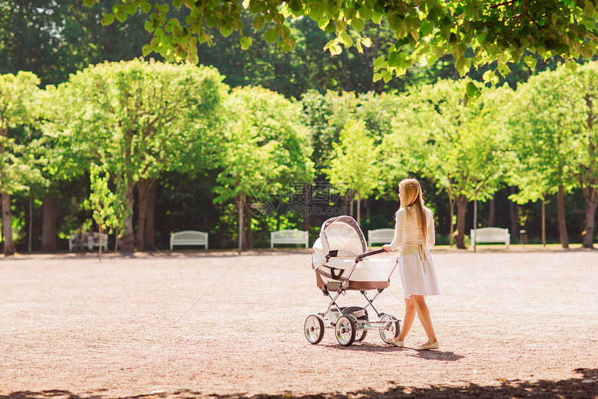 家庭,孩子父母的快乐的母亲与婴儿车公园后走图片