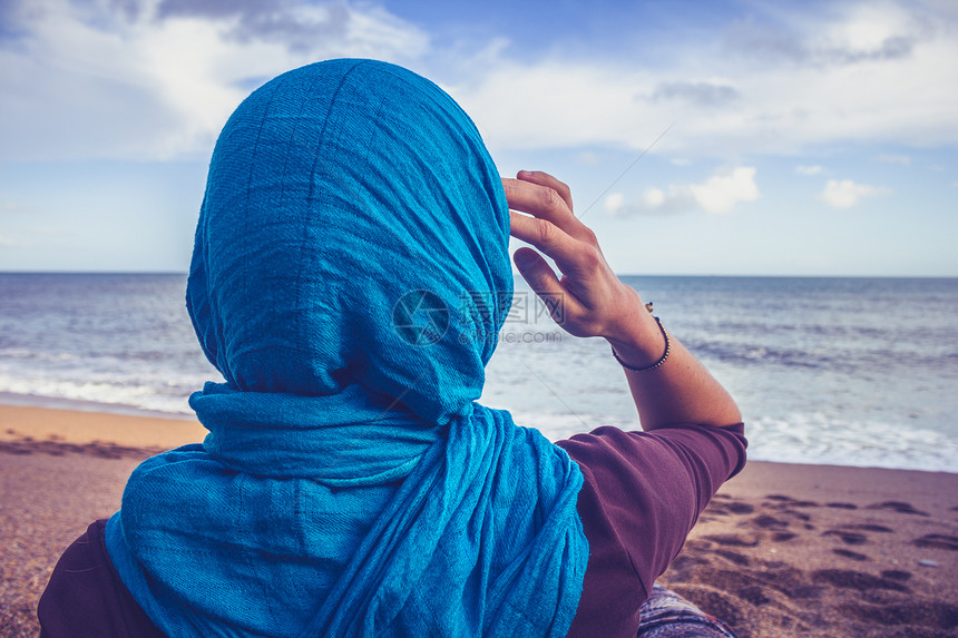 轻的女人戴着头巾海滩上看着大海图片