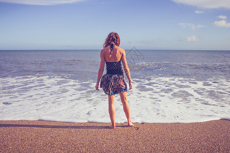轻的女人站海滩上浸脚图片