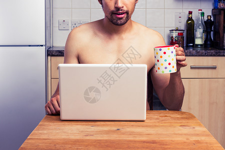 轻的赤膊男子喝茶,笔记本电脑上工作图片