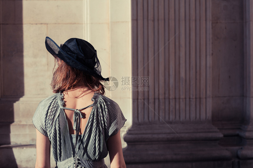 轻的女人穿着优雅的衣服帽子,站个令人印象深刻雄伟的大厅沐浴阳光下图片